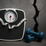 Scale and running shoes symbolizing overcoming a weight loss plateau beyond diet and cardio