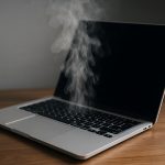 MacBook with overheating warning on screen and heat waves rising from the keyboard
